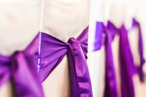 White wedding chairs decorated with purple bows