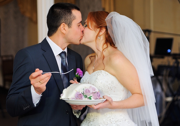Bride and groom feed each other by wedding cake and kissing