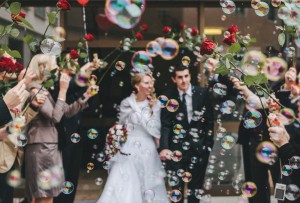 friends celebrating just married couple with soap bubbles and red roses